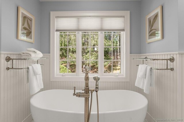 bathroom with a wainscoted wall, plenty of natural light, and a freestanding tub