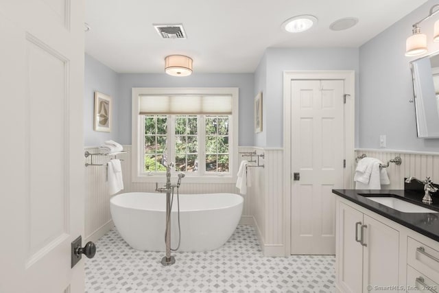 bathroom with a wainscoted wall, tile patterned floors, a freestanding bath, and vanity