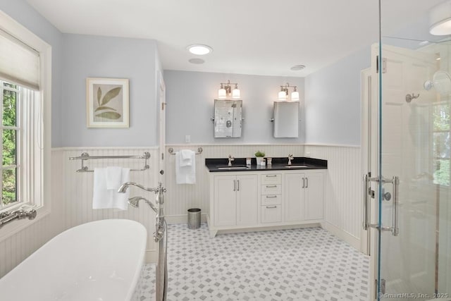 bathroom featuring wainscoting, a shower stall, tile patterned floors, a freestanding tub, and double vanity