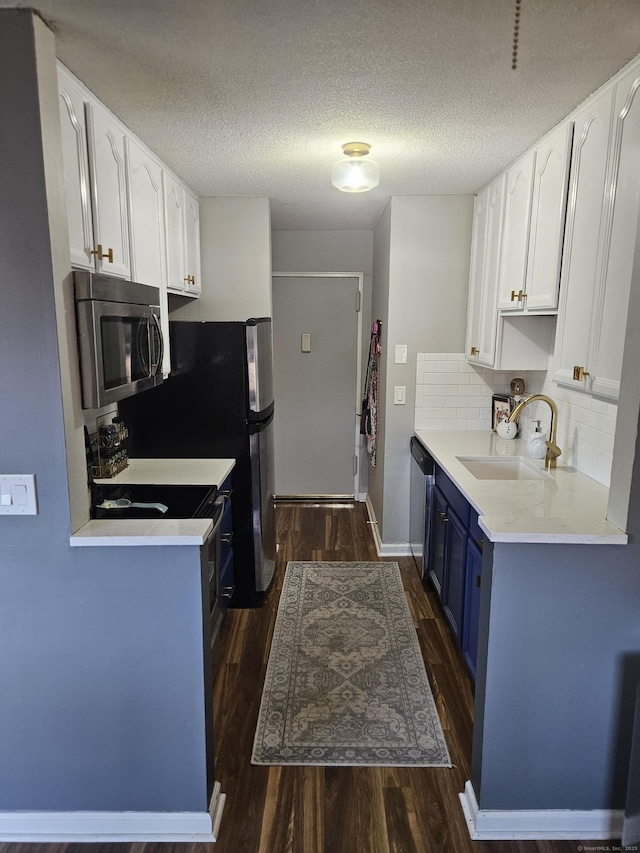 kitchen with white cabinets, appliances with stainless steel finishes, a sink, blue cabinetry, and dark wood-type flooring