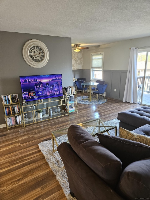 living room with a textured ceiling, ceiling fan, wood finished floors, and a wainscoted wall