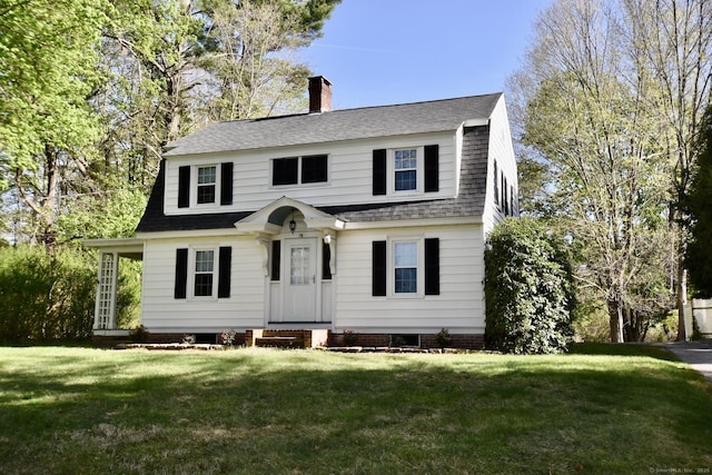 colonial inspired home with a shingled roof, a front lawn, a gambrel roof, and a chimney