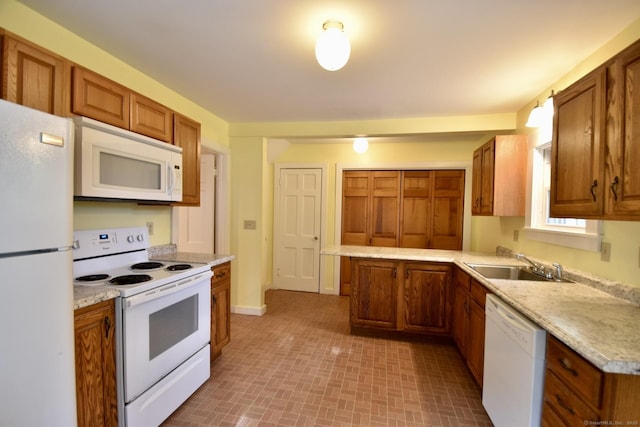 kitchen featuring brown cabinets, a sink, white appliances, a peninsula, and baseboards