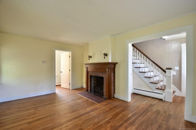 unfurnished living room featuring crown molding, stairs, a brick fireplace, wood finished floors, and baseboard heating
