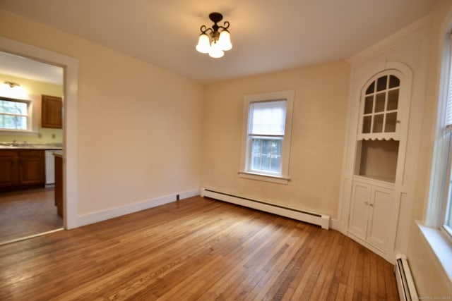 unfurnished dining area with a wealth of natural light, a baseboard heating unit, a baseboard radiator, light wood-style flooring, and a notable chandelier