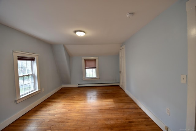 empty room featuring baseboards, baseboard heating, wood finished floors, and a wealth of natural light