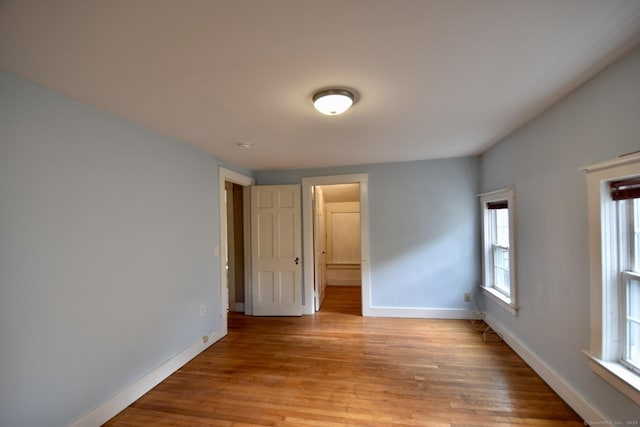 unfurnished bedroom with connected bathroom, baseboards, multiple windows, and light wood finished floors
