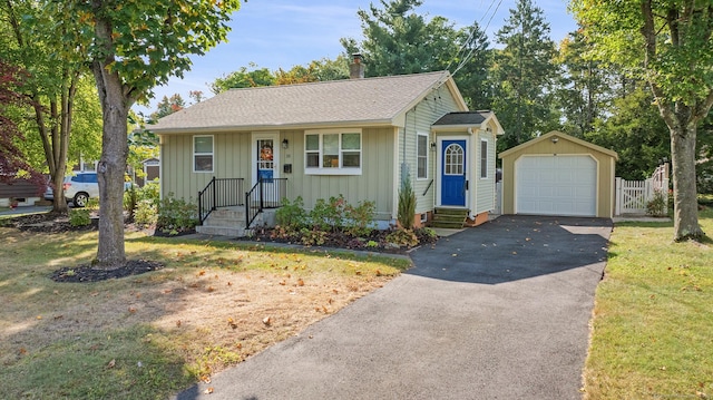 bungalow with aphalt driveway, an outdoor structure, a detached garage, a chimney, and board and batten siding