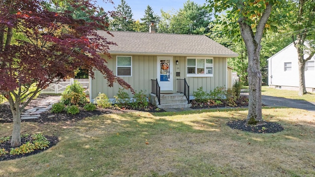 view of front of house featuring board and batten siding, fence, a shingled roof, and a front lawn