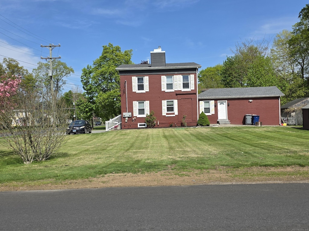 view of front facade featuring a chimney, brick siding, and a front yard