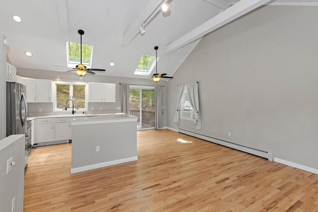kitchen with beam ceiling, light wood-style floors, ceiling fan, baseboard heating, and white cabinetry