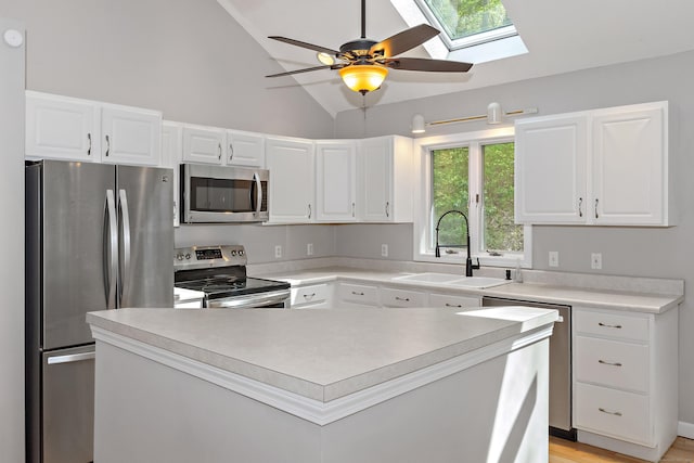 kitchen featuring ceiling fan, white cabinetry, vaulted ceiling with skylight, a sink, and stainless steel appliances