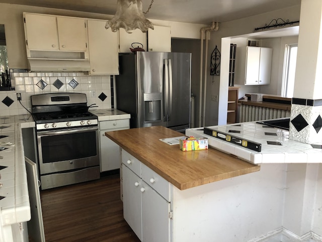 kitchen with appliances with stainless steel finishes, tasteful backsplash, range hood, tile counters, and dark wood-type flooring