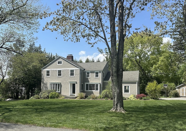 view of front of property with roof with shingles, a chimney, and a front yard