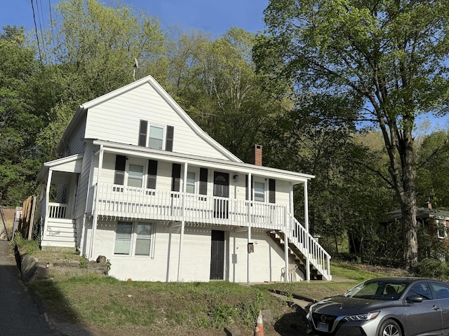 view of front facade featuring a chimney, covered porch, and stairway