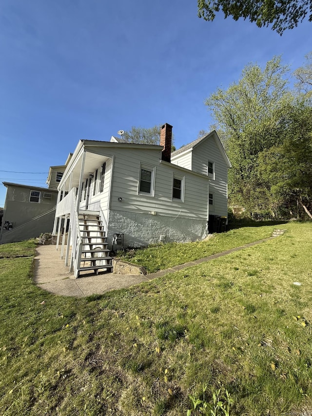 rear view of property featuring a chimney, a yard, and stairway