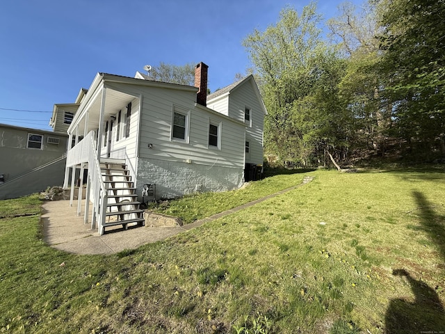 rear view of property featuring a lawn, stairs, and a chimney