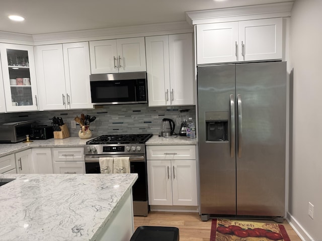 kitchen with light wood-type flooring, appliances with stainless steel finishes, backsplash, and white cabinets