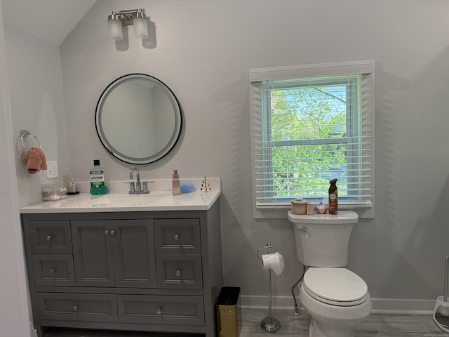 bathroom featuring baseboards, lofted ceiling, toilet, and vanity