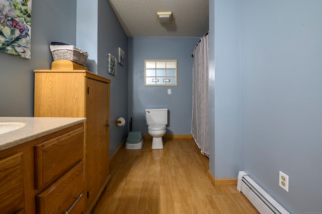 bathroom with baseboard heating, wood finished floors, vanity, baseboards, and toilet