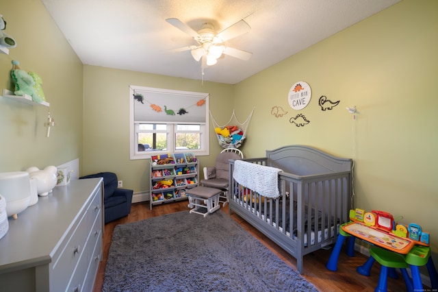 bedroom featuring a nursery area, ceiling fan, and wood finished floors