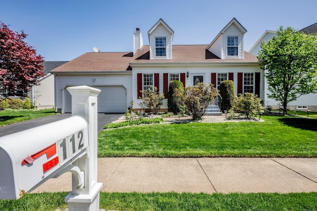 new england style home with an attached garage, a chimney, a front lawn, and aphalt driveway