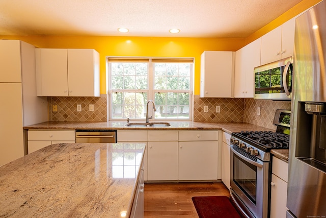 kitchen featuring appliances with stainless steel finishes, tasteful backsplash, light stone countertops, wood finished floors, and a sink