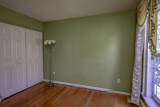 unfurnished bedroom with baseboard heating, baseboards, wood finished floors, and a closet