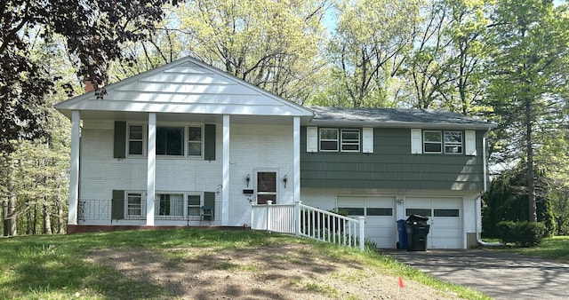 split foyer home with an attached garage, aphalt driveway, brick siding, and a porch