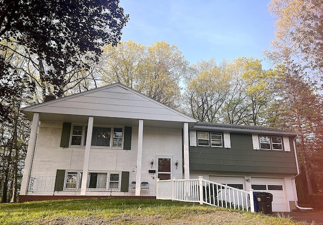 raised ranch with an attached garage, covered porch, and brick siding