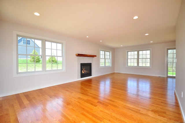 unfurnished living room featuring light wood-style floors, baseboards, recessed lighting, and a tile fireplace