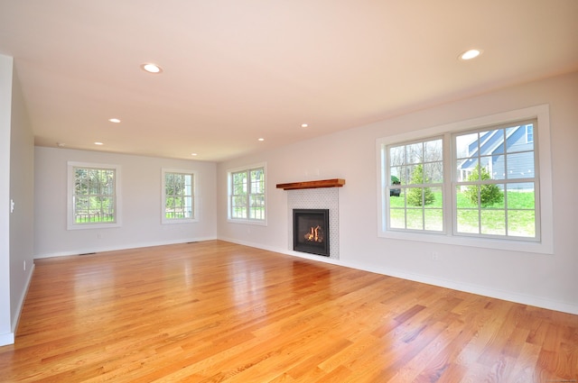 unfurnished living room featuring recessed lighting, light wood finished floors, a glass covered fireplace, and baseboards