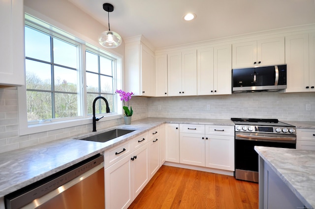 kitchen with light stone countertops, a sink, light wood finished floors, stainless steel appliances, and white cabinetry