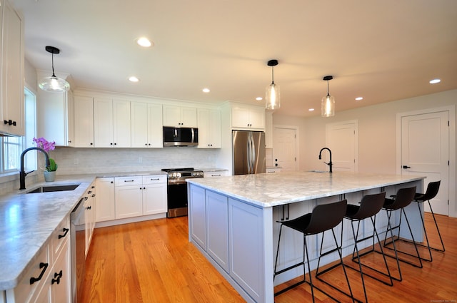 kitchen featuring white cabinets, stainless steel appliances, a sink, and light wood finished floors