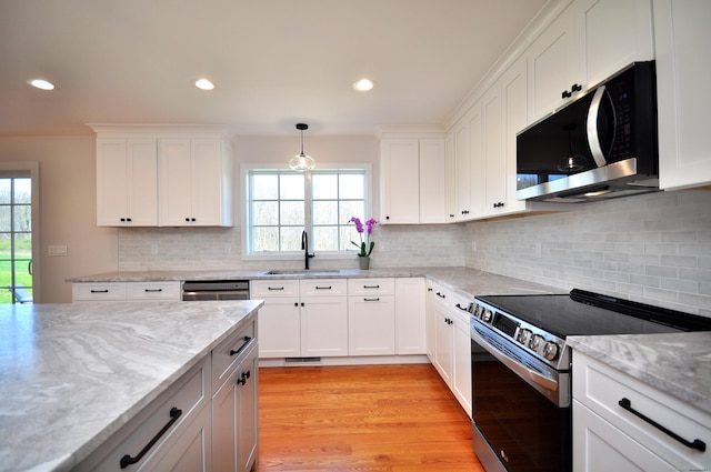 kitchen with a sink, appliances with stainless steel finishes, white cabinets, and light stone counters