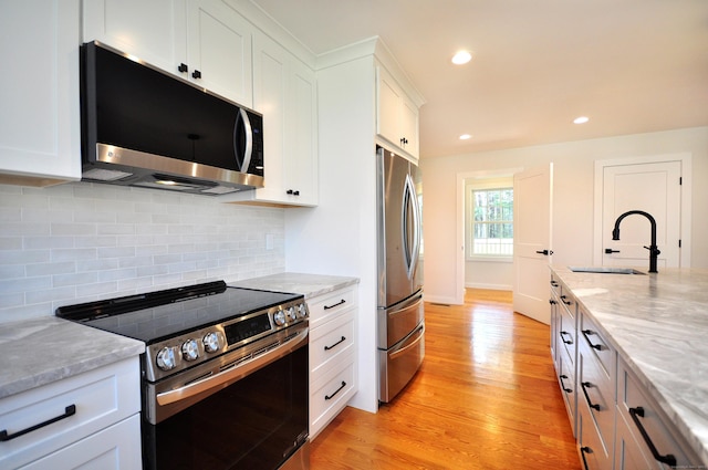 kitchen with a sink, stainless steel appliances, light wood-style flooring, and white cabinetry