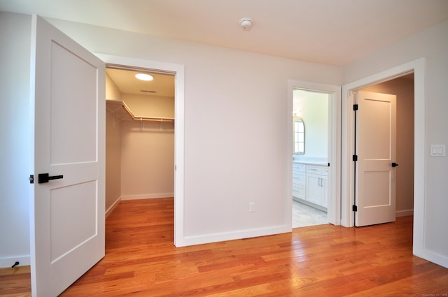 unfurnished bedroom with light wood-type flooring, baseboards, a walk in closet, and a closet