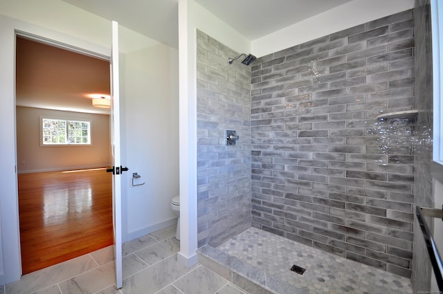 bathroom featuring toilet, baseboards, a tile shower, and marble finish floor