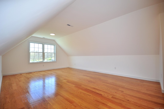 additional living space featuring baseboards, vaulted ceiling, light wood-style flooring, and visible vents