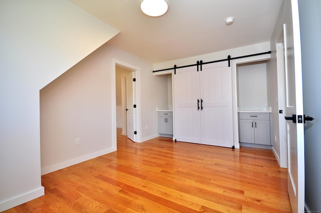 unfurnished bedroom with baseboards, a barn door, and light wood-style flooring
