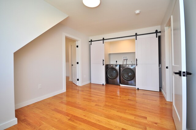clothes washing area featuring laundry area, a barn door, separate washer and dryer, baseboards, and light wood-type flooring