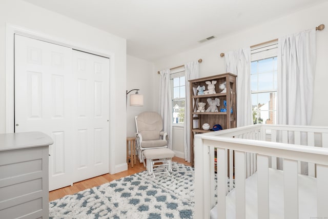 bedroom with a crib, a closet, light wood finished floors, and visible vents