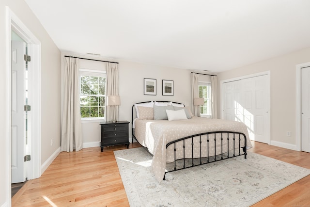 bedroom featuring baseboards, two closets, light wood-style flooring, and visible vents