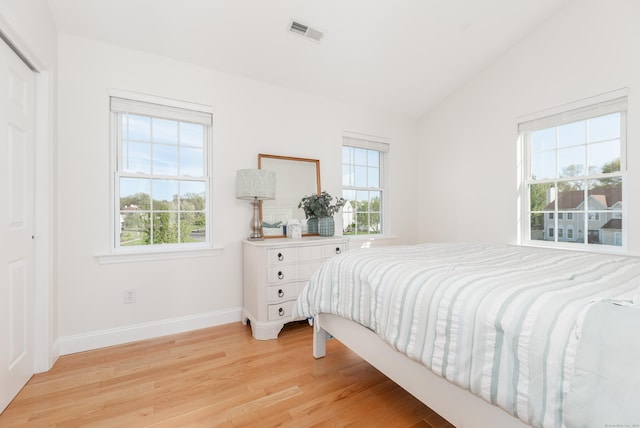 bedroom with baseboards, lofted ceiling, light wood finished floors, and visible vents