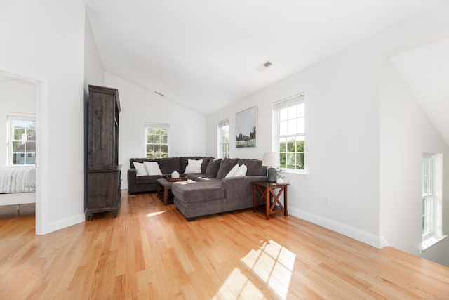 living area with visible vents, light wood-style floors, baseboards, and vaulted ceiling
