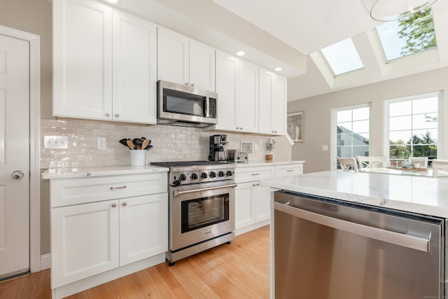 kitchen featuring white cabinets, appliances with stainless steel finishes, light wood-style flooring, decorative backsplash, and a skylight
