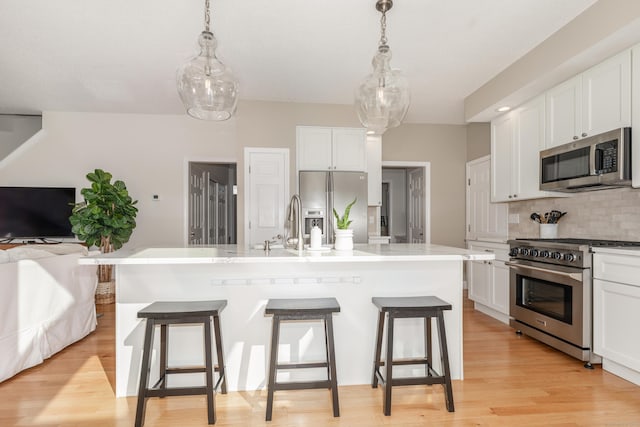 kitchen featuring appliances with stainless steel finishes, tasteful backsplash, white cabinetry, open floor plan, and a kitchen bar