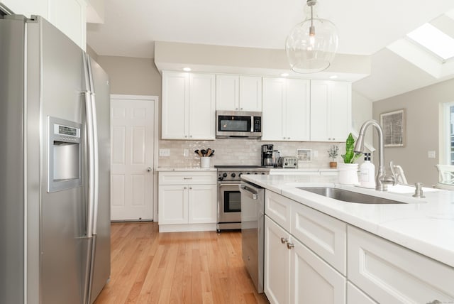 kitchen with decorative backsplash, a sink, white cabinets, light wood-style floors, and stainless steel appliances