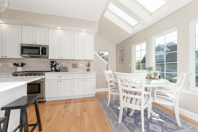 kitchen with stainless steel appliances, tasteful backsplash, lofted ceiling with skylight, and light wood-style floors