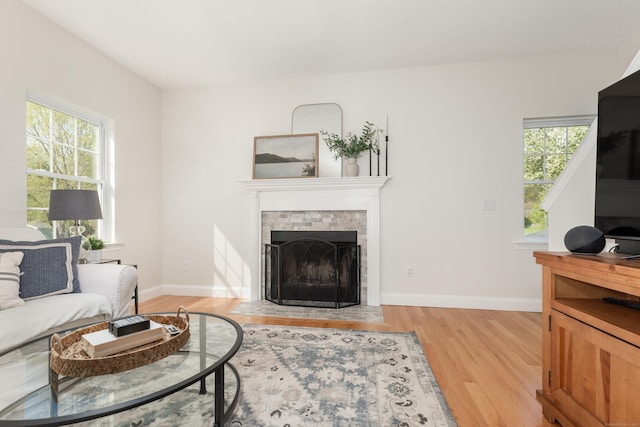living area featuring baseboards, a tile fireplace, plenty of natural light, and light wood-type flooring